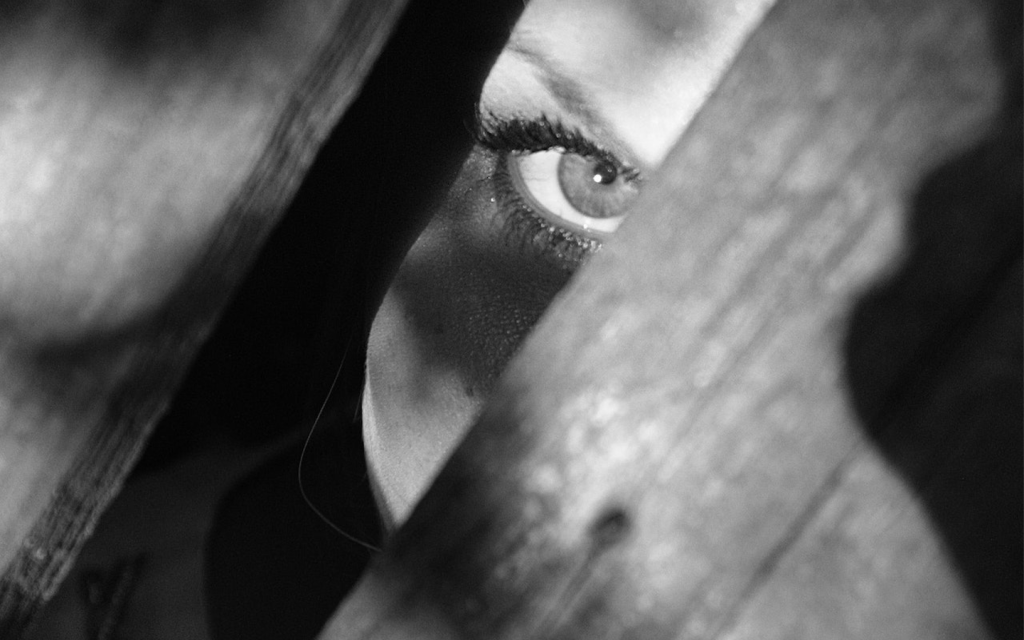 This is a black and white photography with a White woman's menacing eye peaking through the cracks of a wooden surface, signifying the very real threat of Amma in "Sharp Objects".