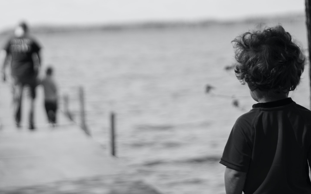 This is an adult with a young child walking on a dock towards a large body of water while another kid watches on to the right of the frame as though they had been left behind, representing the forgetten and neglected children in "Capernaum".