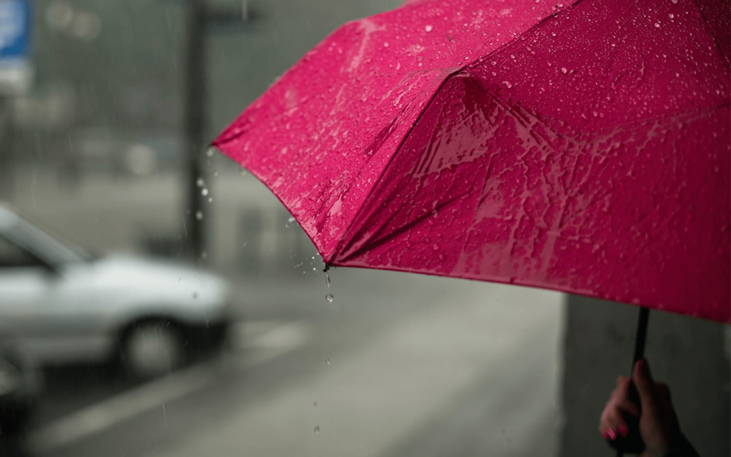 This is a red umbrella drenched in rain with a woman's rain painted nailed hand just in frame at the corner right of the picture. To the left of the frame is a grey blurred car parked by a light pole. This represents Yoon Jin ah in "Something in the Rain", and particularly, her umbrella in the show.