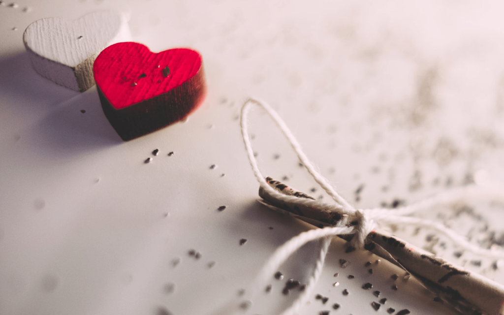 This is a wood carved blocked heart and a white carved heart on a white glittered surface. It features a branch with a string tied in a ribbon. This represents the romance ien "Extraordinary You".