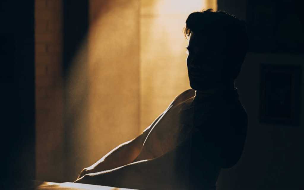 This is a man sitting in the shadowed section of a rom with light shining down from above, just behind him. This represents the invisible man in the movie.