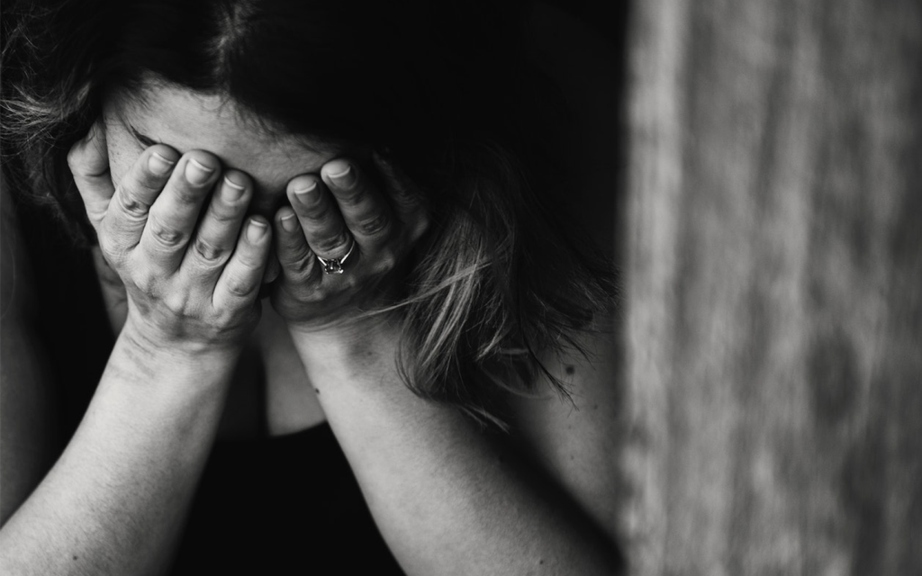 This is a white and black image of a woman with her hand over her eyes, standing beside the trunk of a tree. This represents Lenu is "My Brilliant Friend" seaso 2 episode 5.