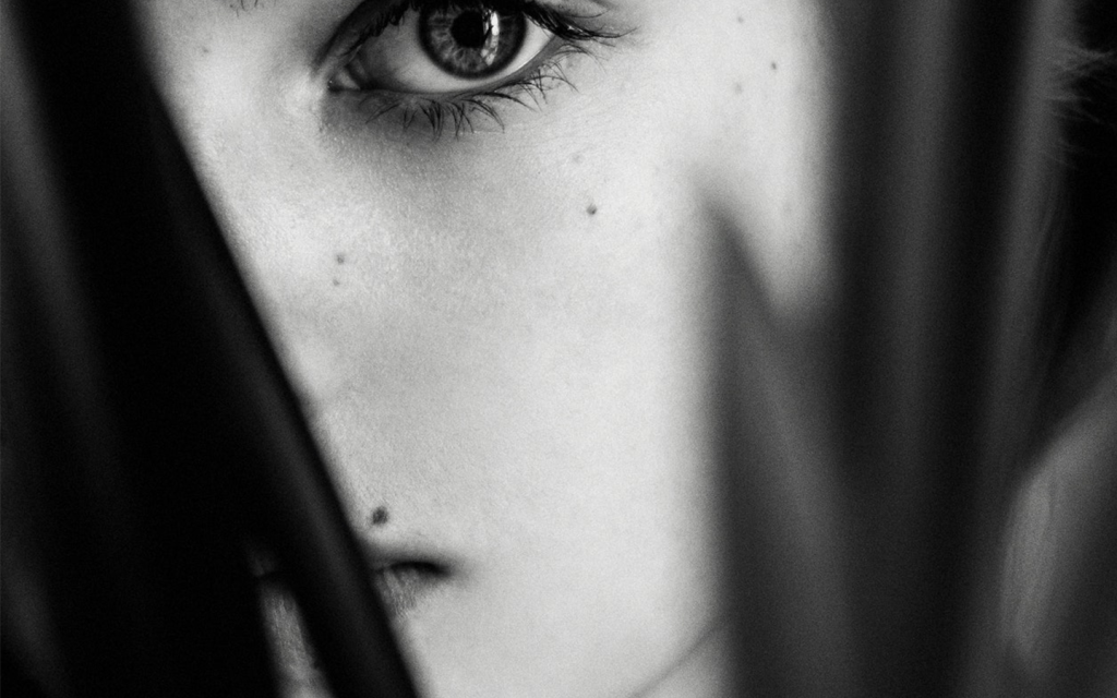 This is a black and white image of a woman's face peaking between plants. The woman looks quite a lot like Adele in "Behind Her Eyes".